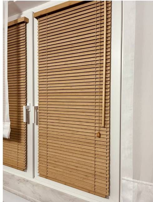 Persianas de madera que cubren una ventana junto a una puerta de cristal cerrada en una habitación de color claro.