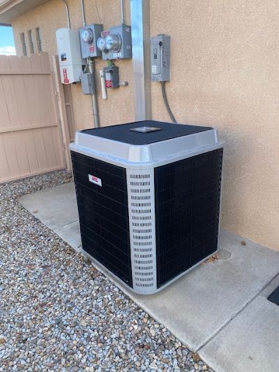 A black air conditioner is sitting on the sidewalk outside of a house.