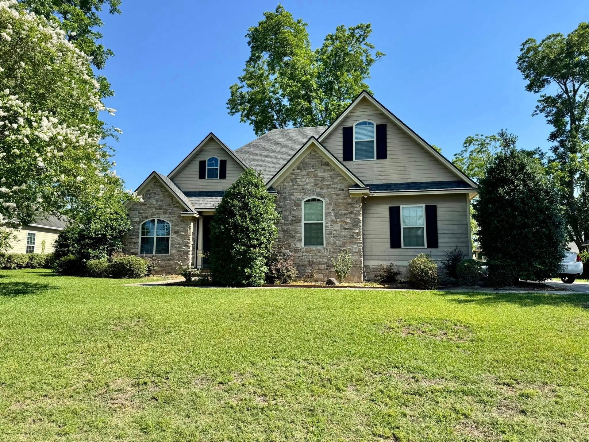 A single-story house with a stone and tan exterior, green lawn, and blue sky.