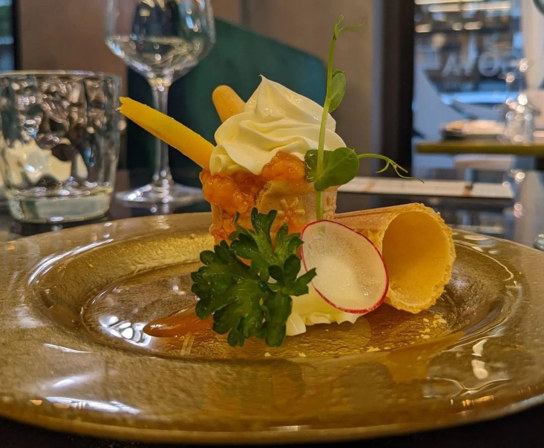 Elegante antipasto servito su un piatto dorato con fiori ed erbe aromatiche commestibili, in un ambiente da ristorante.