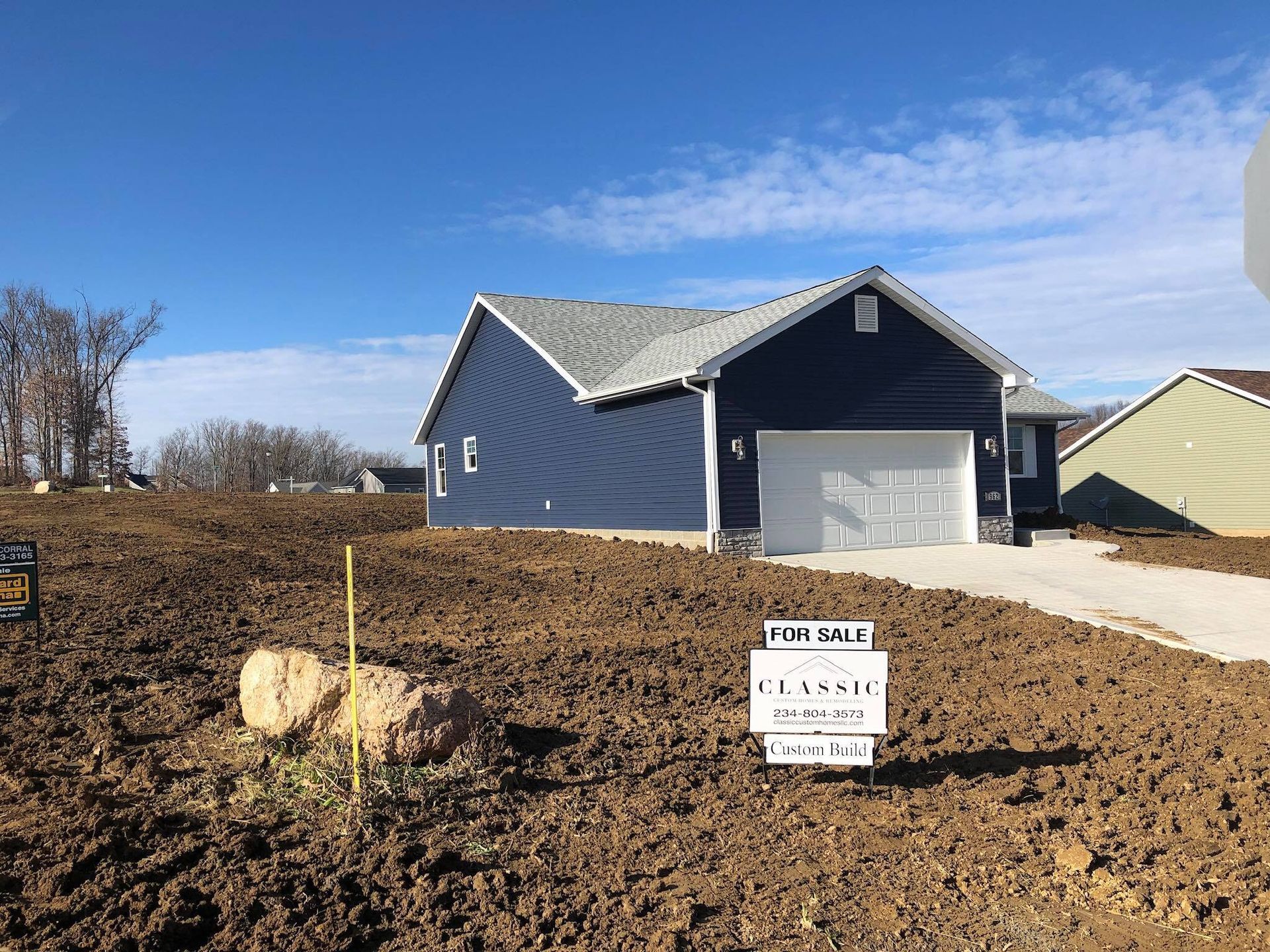 Blue house with attached garage on a bare dirt lot, under a blue sky. 