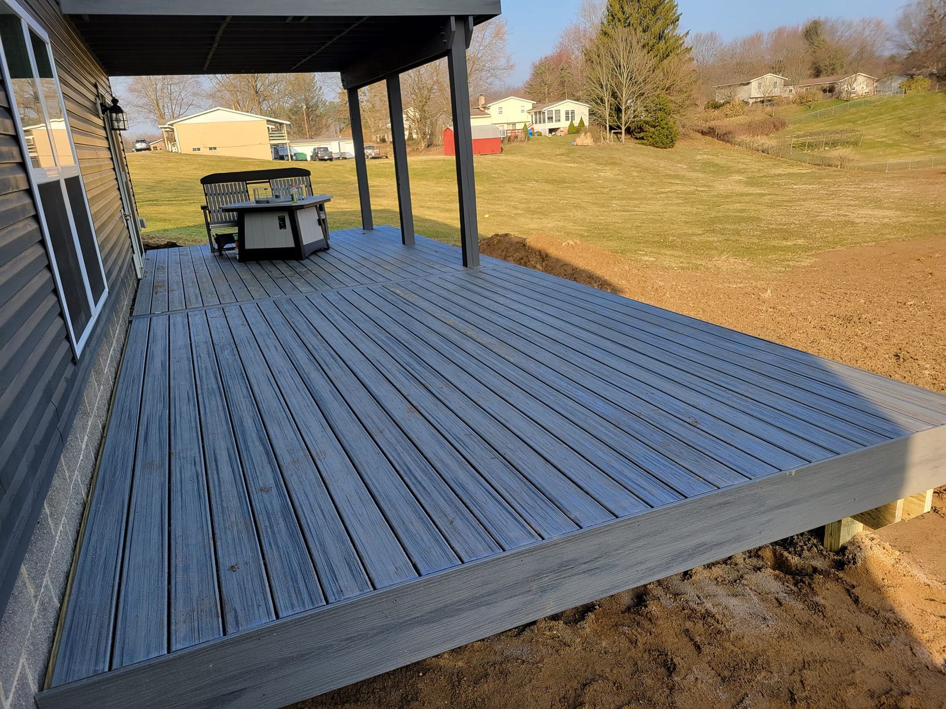 Gray composite deck attached to a building, partially covered, with a small table and a grassy yard.