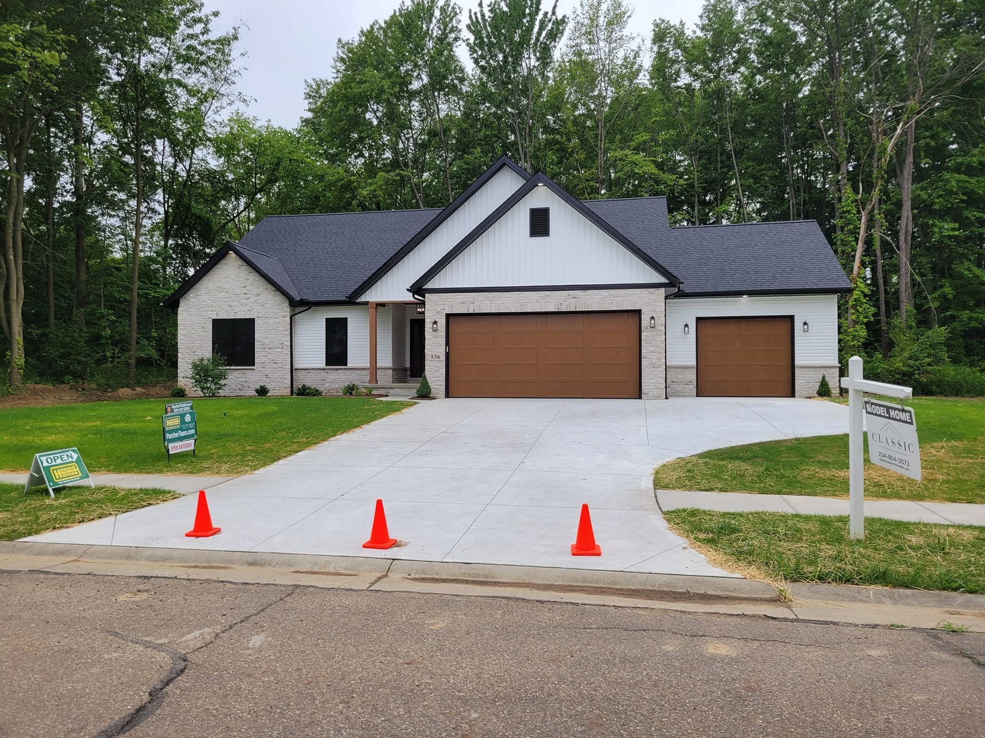 New construction house with tan garage doors, white siding, and brick accents. Orange cones in the driveway.