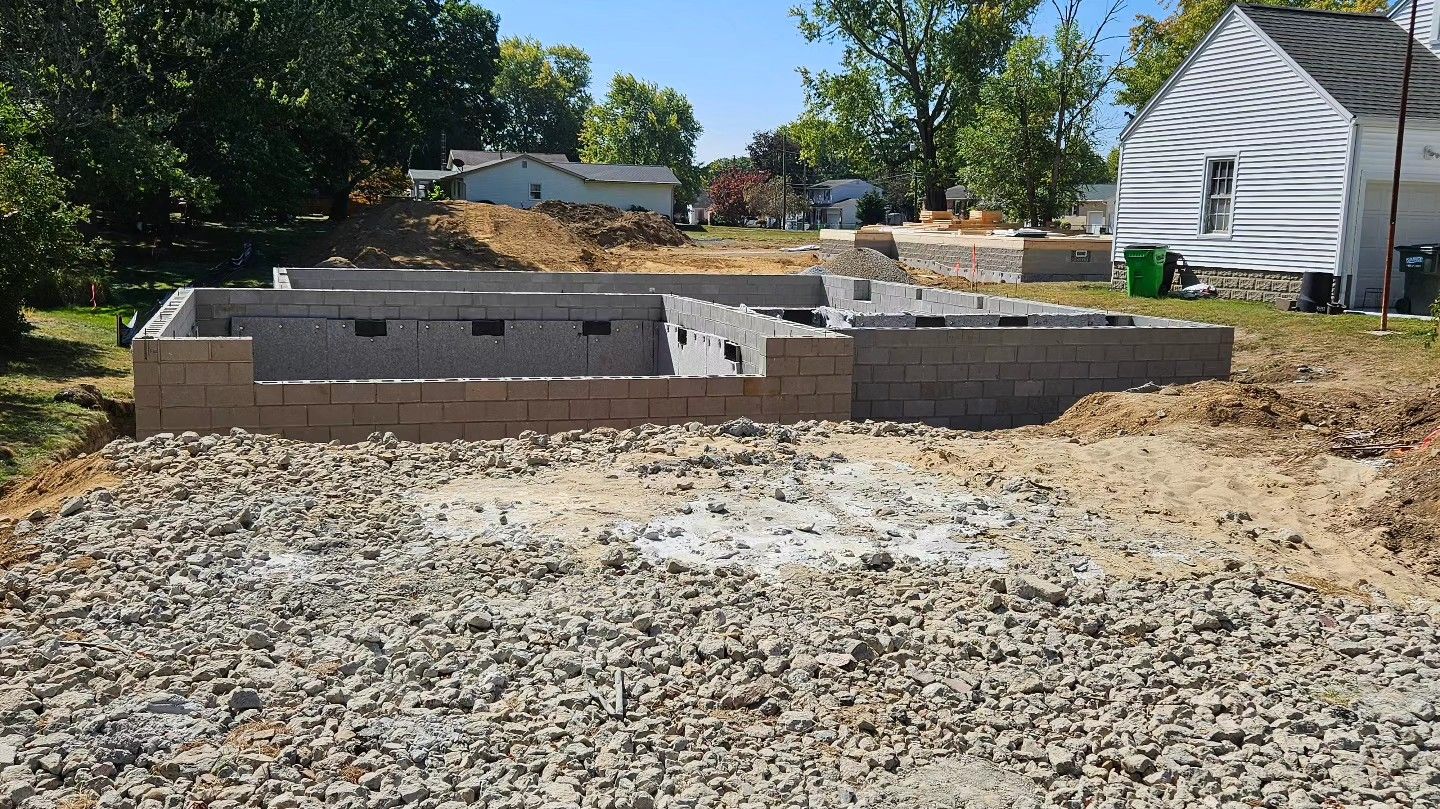 Foundation of a building under construction, grey cinder blocks, gravel ground, and residential setting.