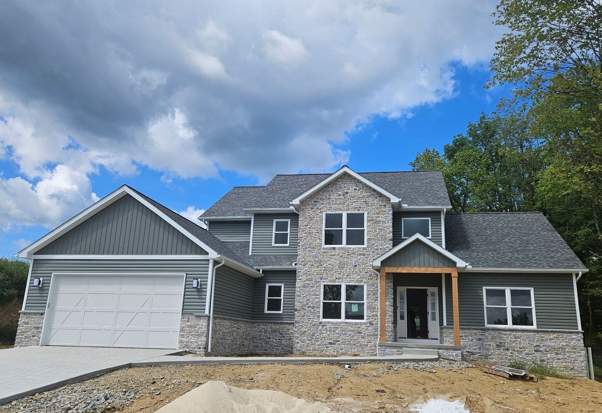 Two-story house with gray roof, stone accents, and attached garage under a cloudy sky.