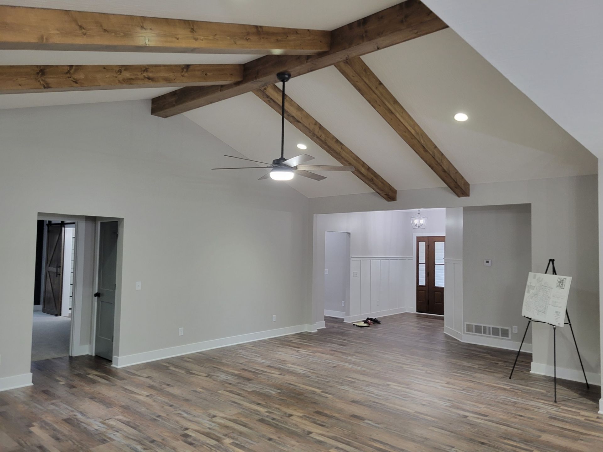 Spacious, empty living room with wood beams, light gray walls, dark wood floors, and a ceiling fan.