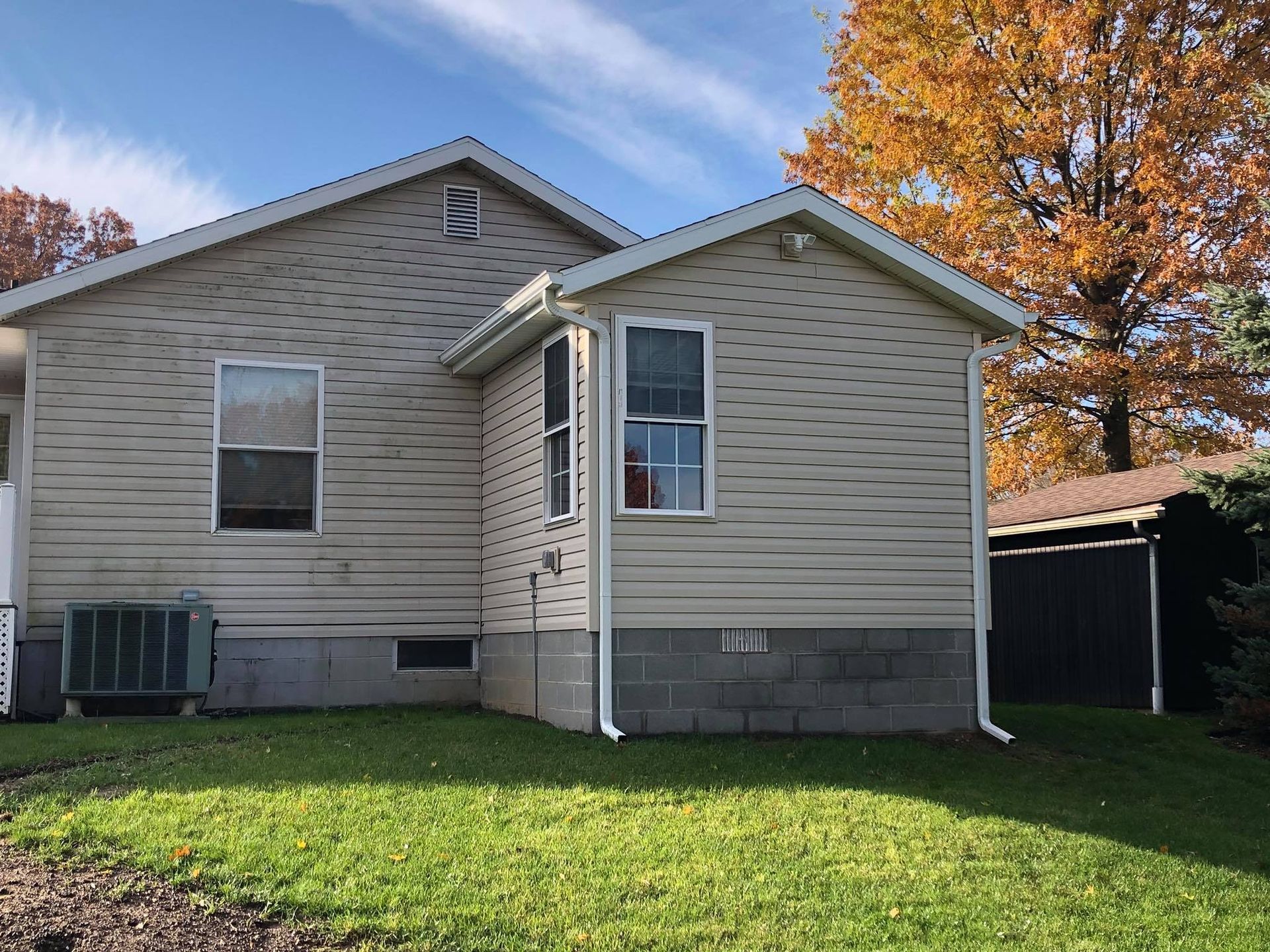 Back of a house with beige siding, a small addition, and fall foliage in the background.