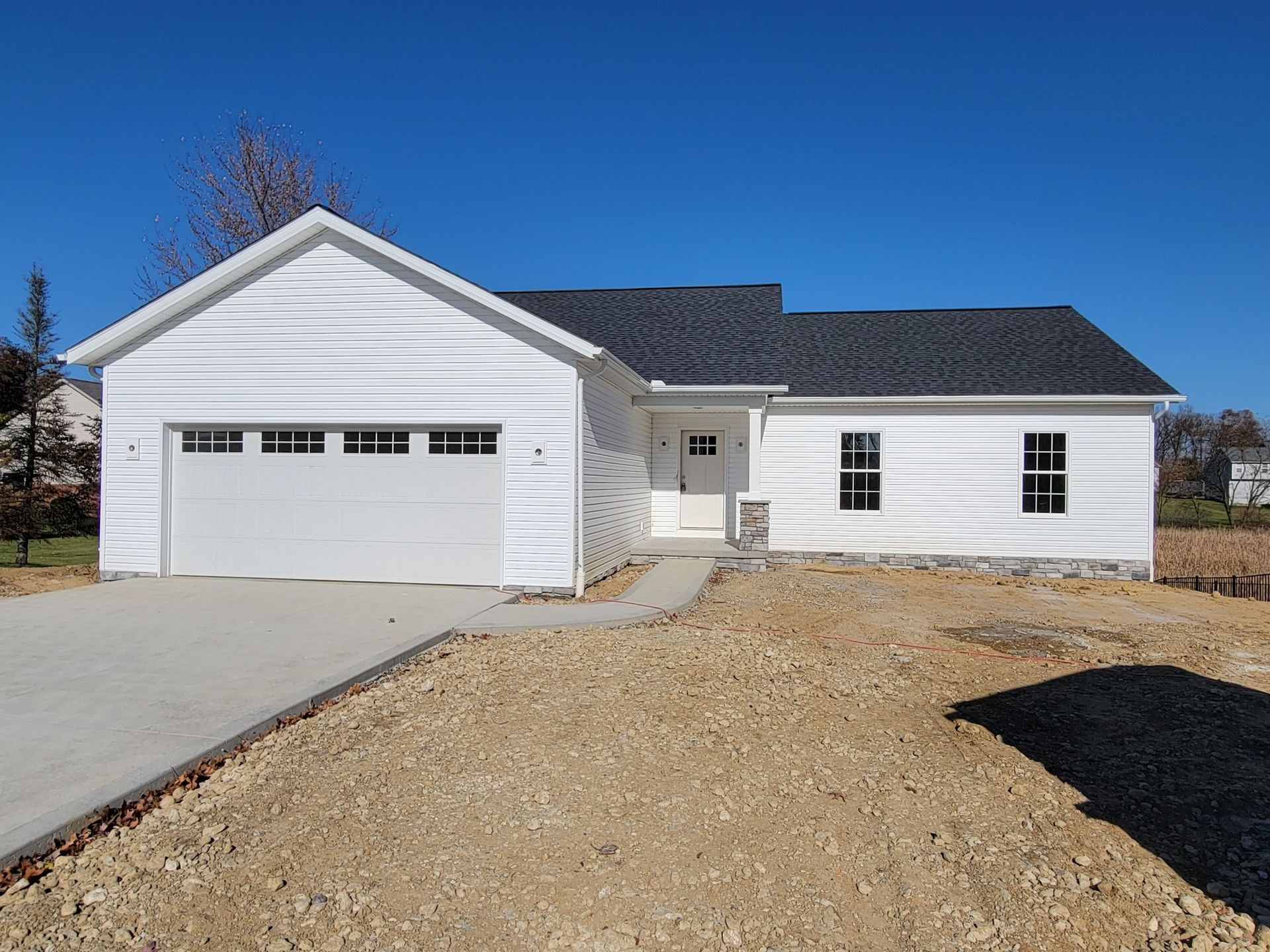 White ranch-style house with a garage, driveway, and bare yard under a blue sky.
