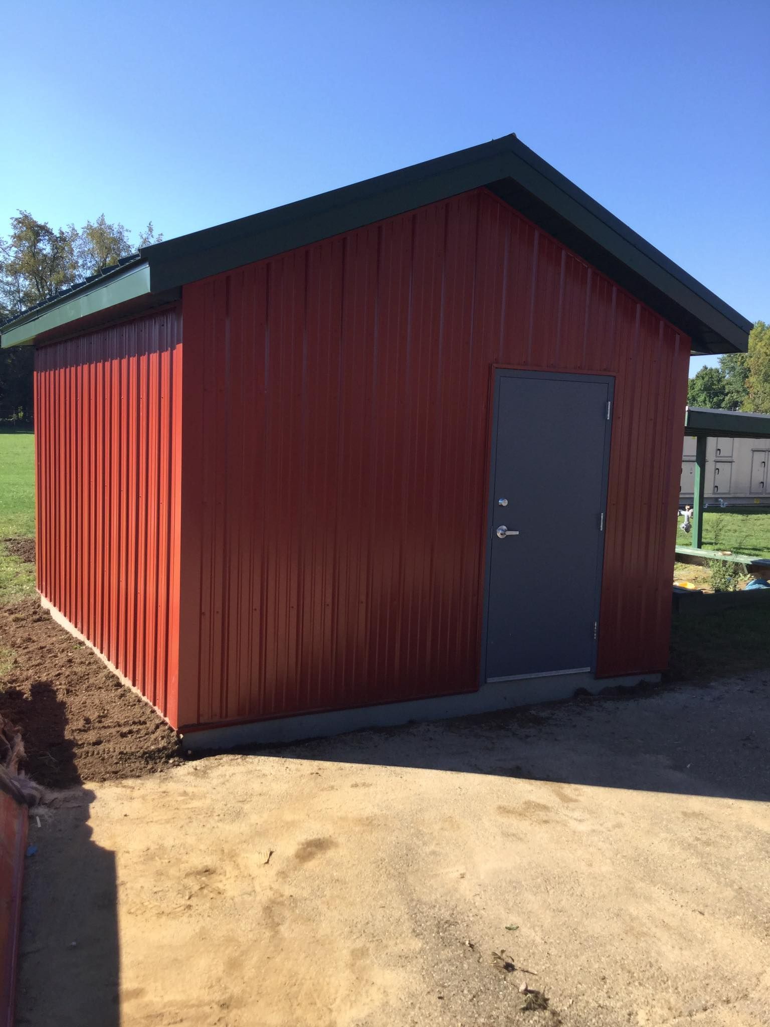 Red metal shed with gray door, set against a blue sky, grass and dirt.