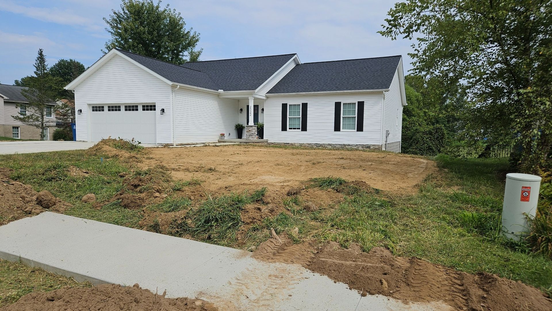 White house with black shutters, unlandscaped yard, new concrete sidewalk.