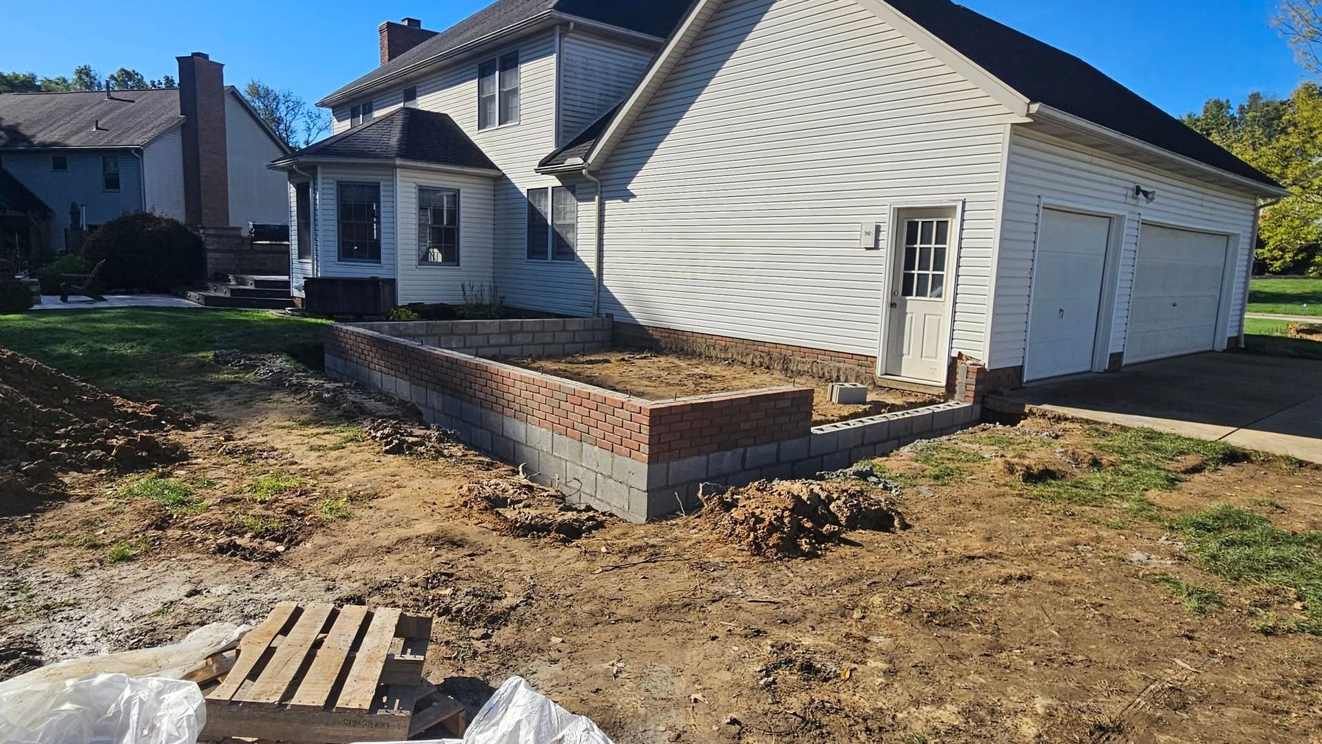 A raised garden bed under construction next to a house with a garage. Dirt surrounds the foundation.