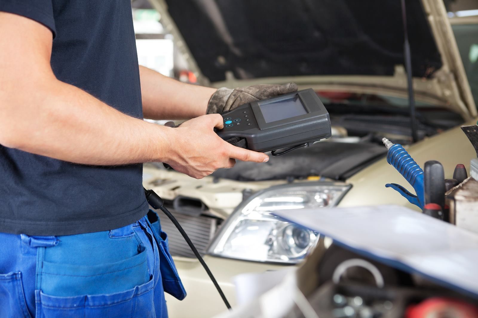Mechanic holding diagnostic tool, inspecting car engine in garage.
