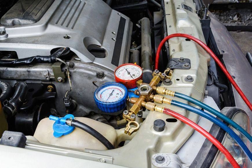 An engine bay with gauges and hoses connected, likely servicing a car's AC system.
