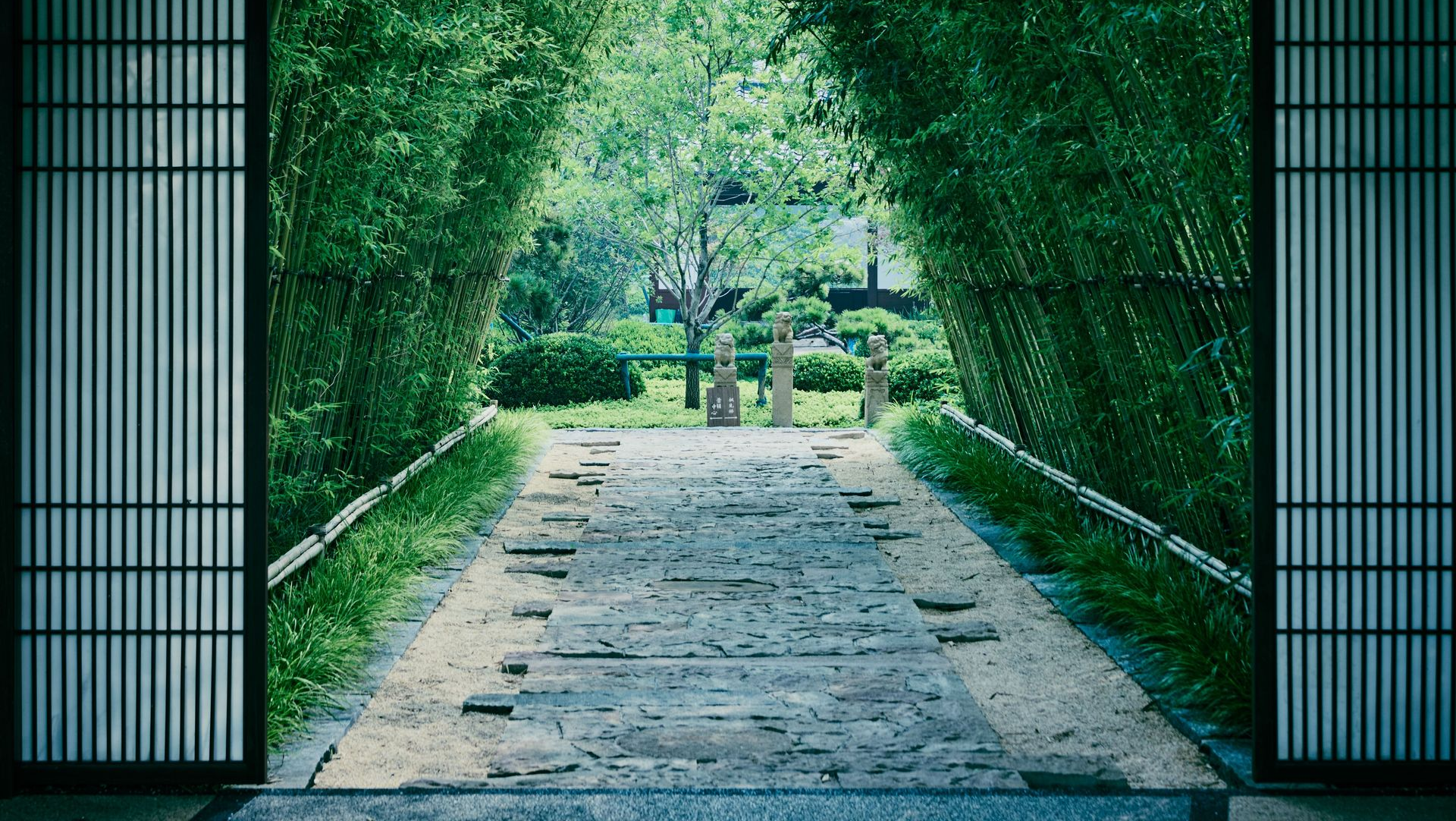 Stone path under a green leafy archway leading to a garden opening, framed by dark gates.