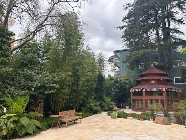A gazebo with flags on it is surrounded by trees and a bench.