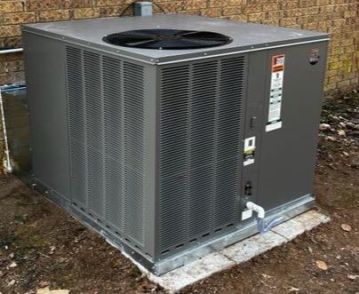 A large air conditioner is sitting on the ground in front of a brick building.