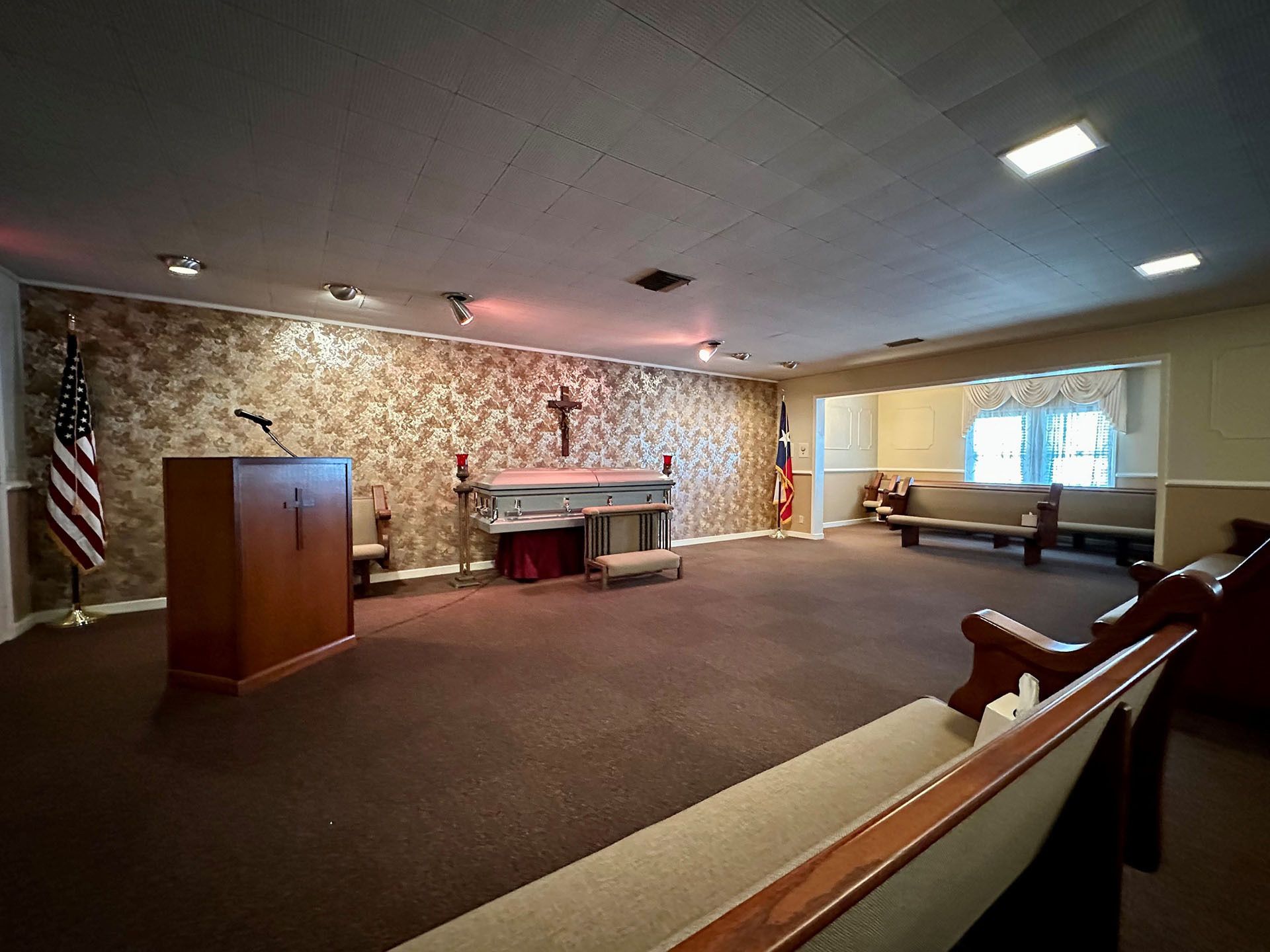 Empty chapel with altar, cross, flags, and pews in a carpeted room