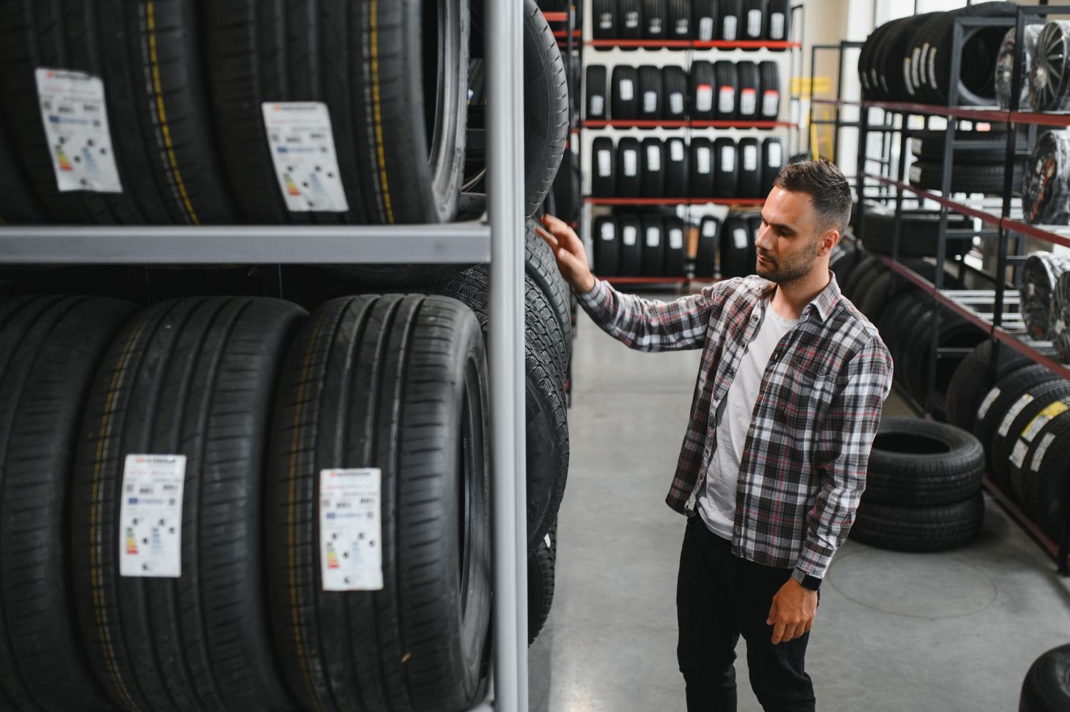 Man examining stacked tires in a warehouse aisle