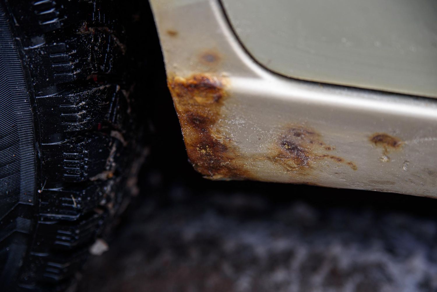 Close-up of a rusted car door panel beside a black tire