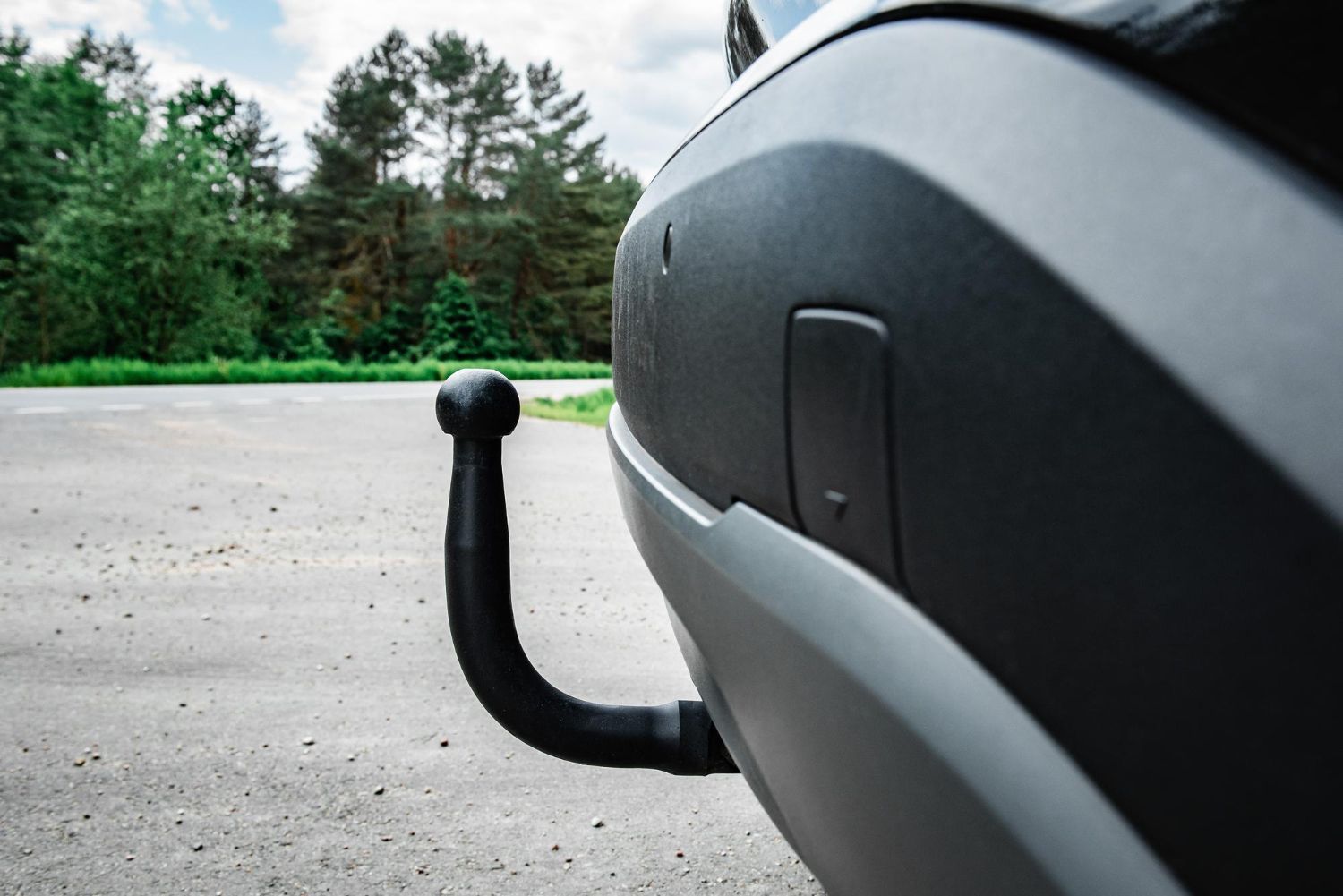 Close-up of a car’s rear tow hitch with a wooded roadside background
