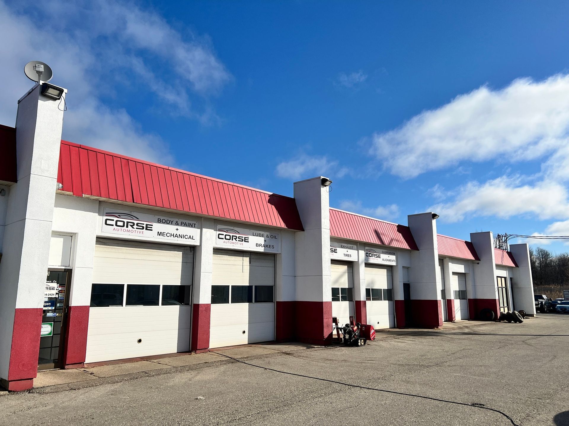Auto repair shop with red roof and trim, white walls, and multiple garage doors under a blue sky.