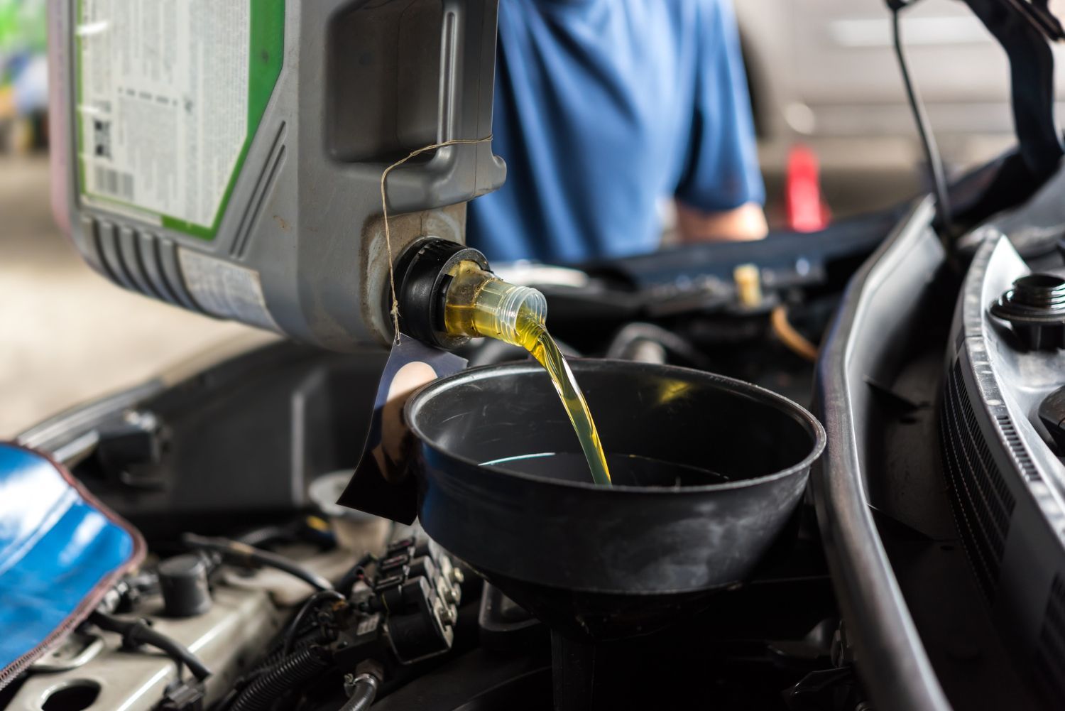 Oil pouring from a car into a black drain pan in a garage