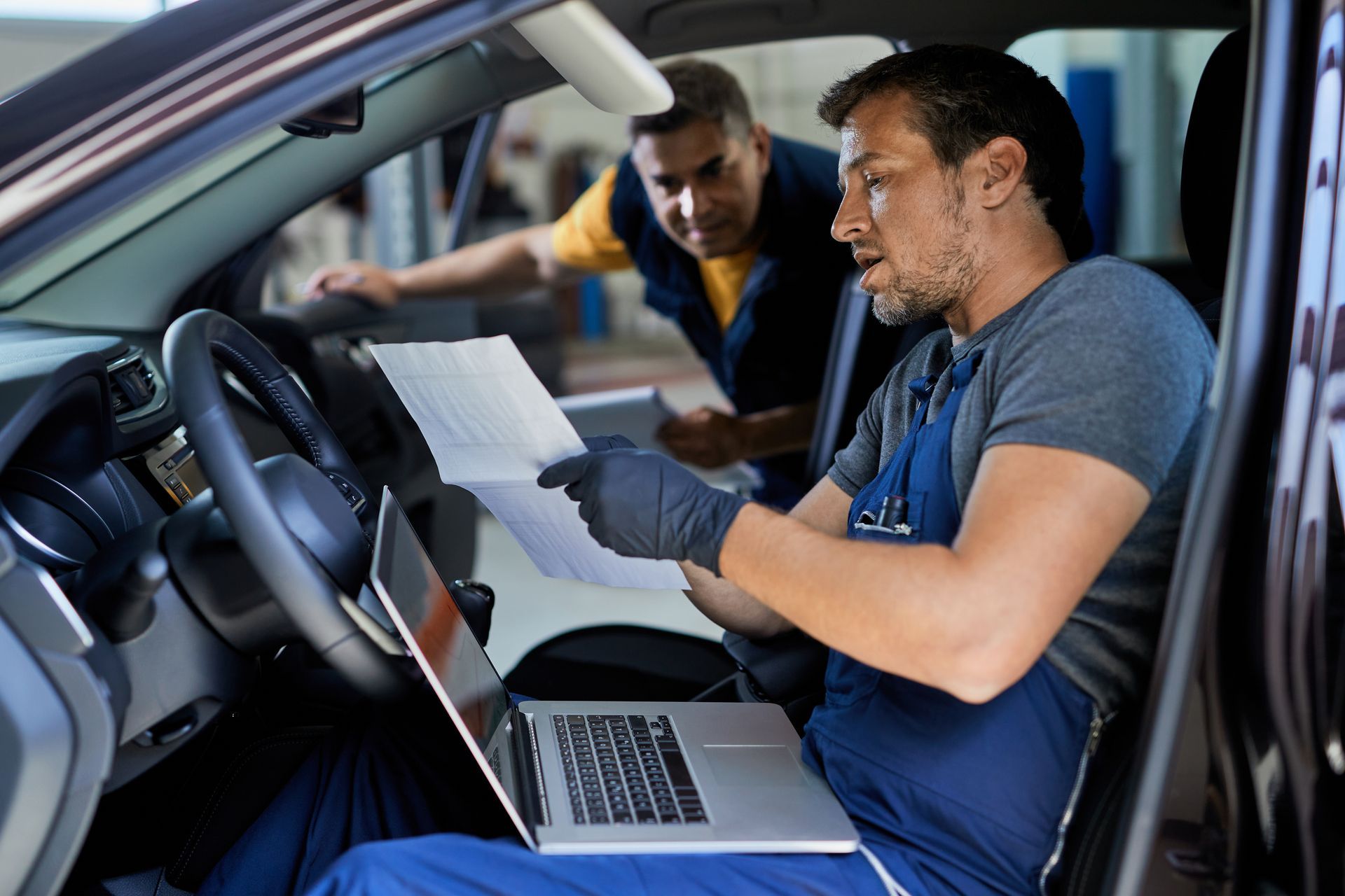 A man is sitting in a car looking at a laptop.