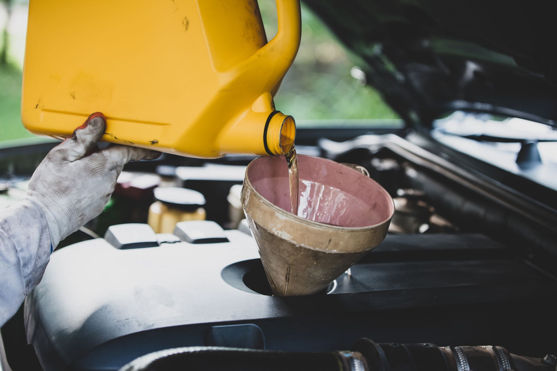 A person is pouring oil into a funnel from a yellow container.