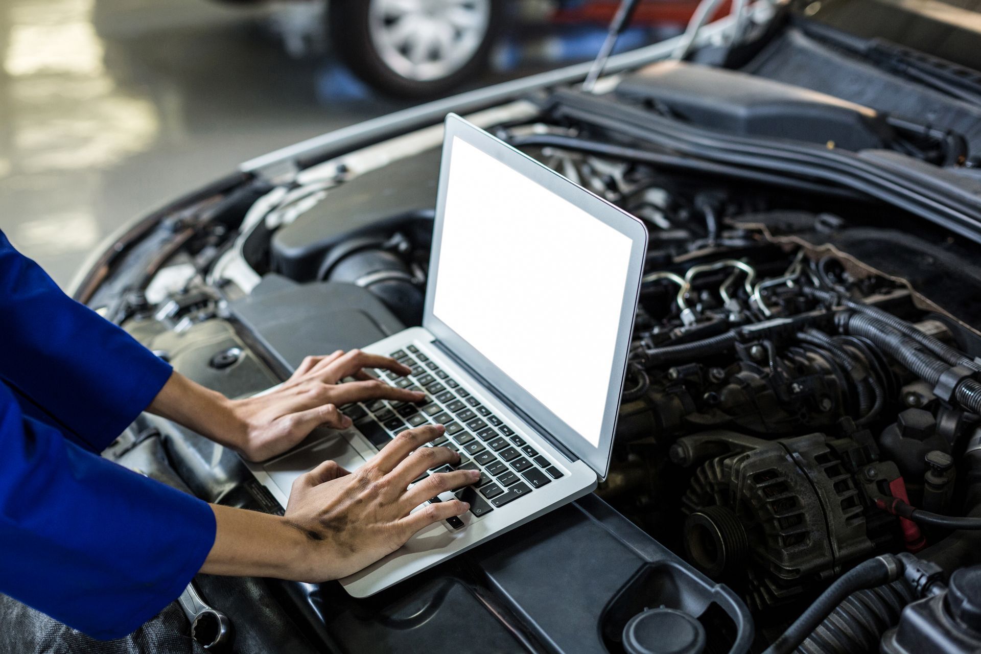 A mechanic is using a laptop computer to check the engine of a car.