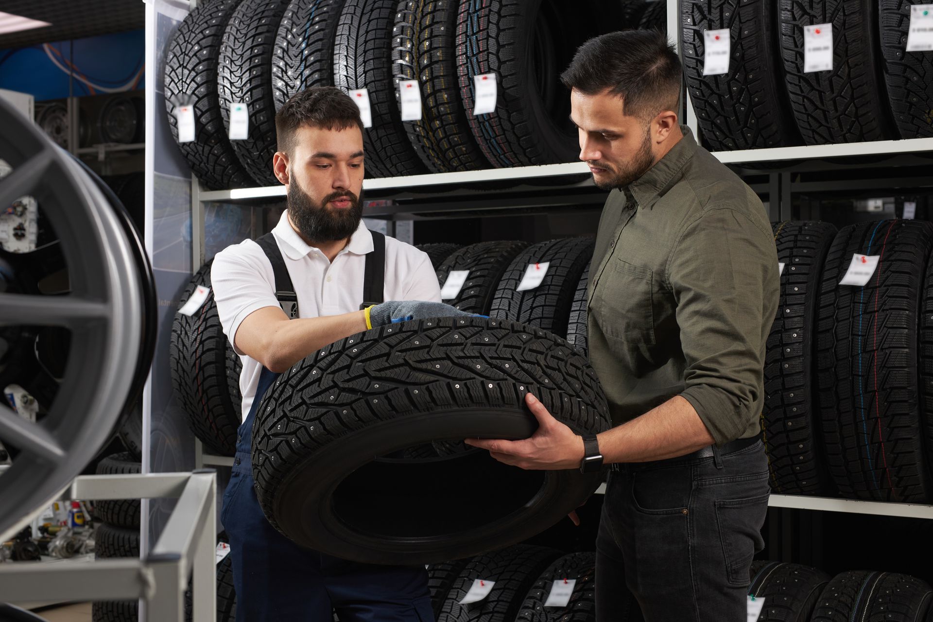 Two men are looking at a tire in a tire store.