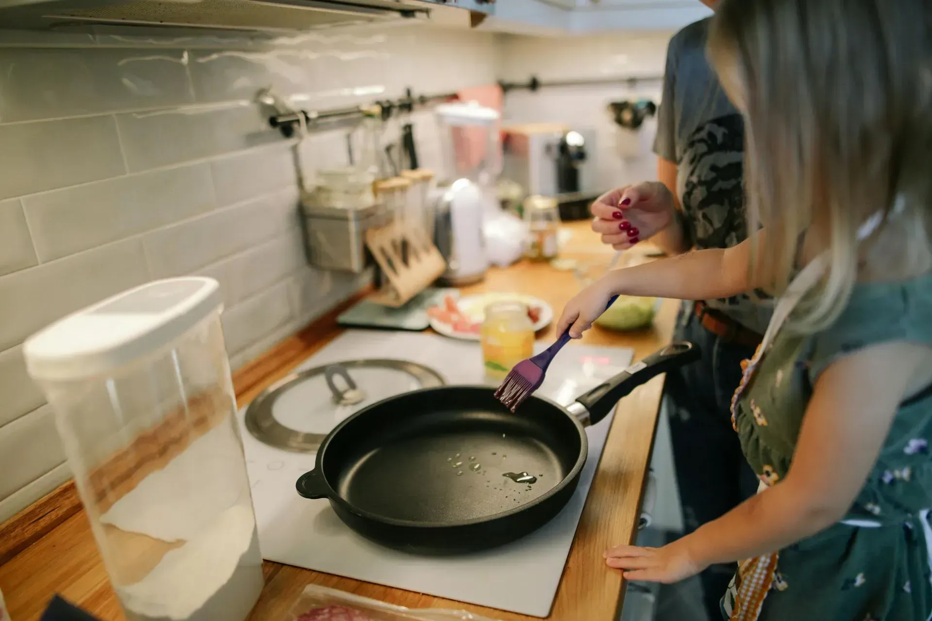 Person cooking in a kitchen, adding oil to a frying pan on the stove.