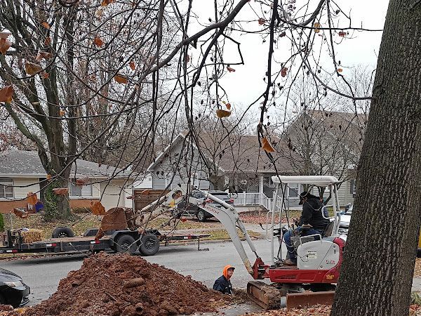 Tree crew working with a cherry picker beside a large dirt pile in a residential street