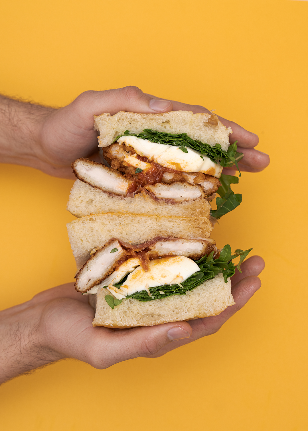 Hands holding the Hot Honey Parm sandwich on a mustard yellow background