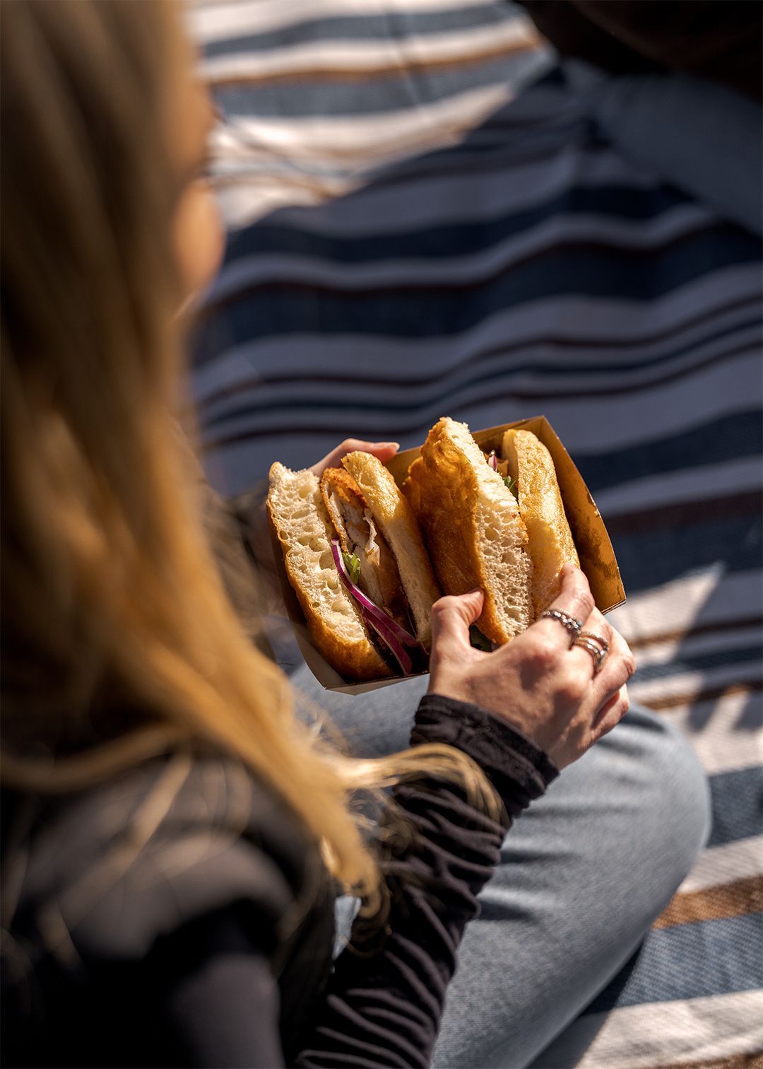 Woman eating a sandwich on a picnic rug