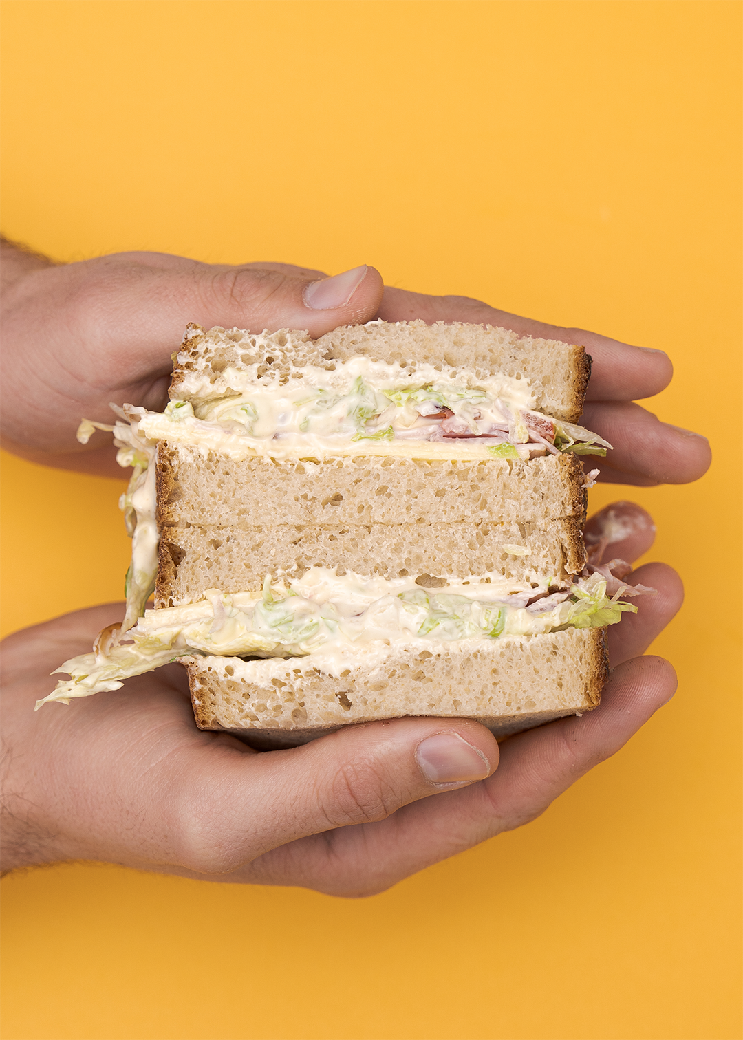 Hands holding the morning mayo sandwich on a mustard yellow background