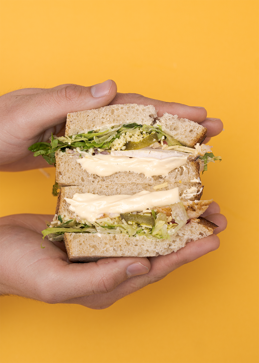 Hands holding the Emperor sandwich on a mustard yellow background