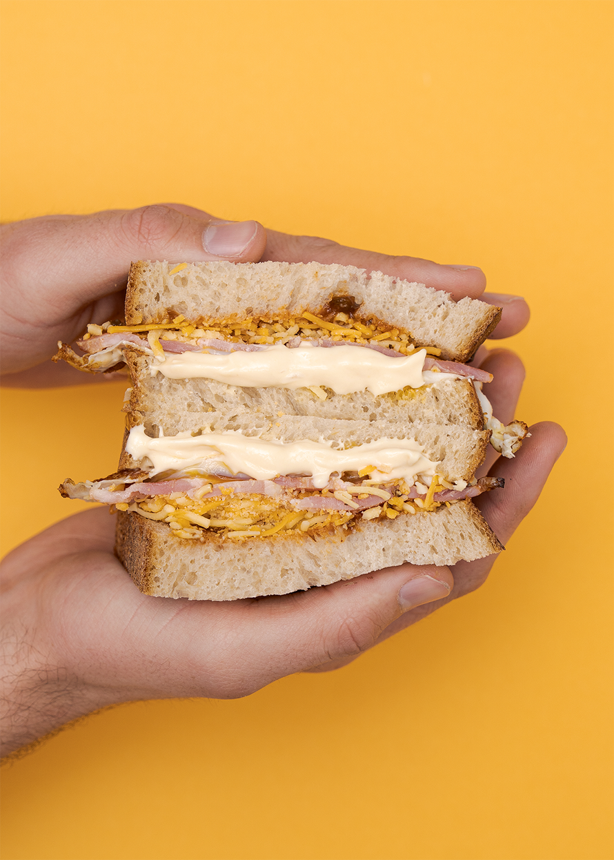 Hands holding the morning mayo sandwich on a mustard yellow background