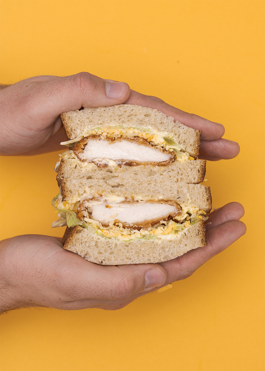 Hands holding The Schnitty sandwich on a mustard yellow background