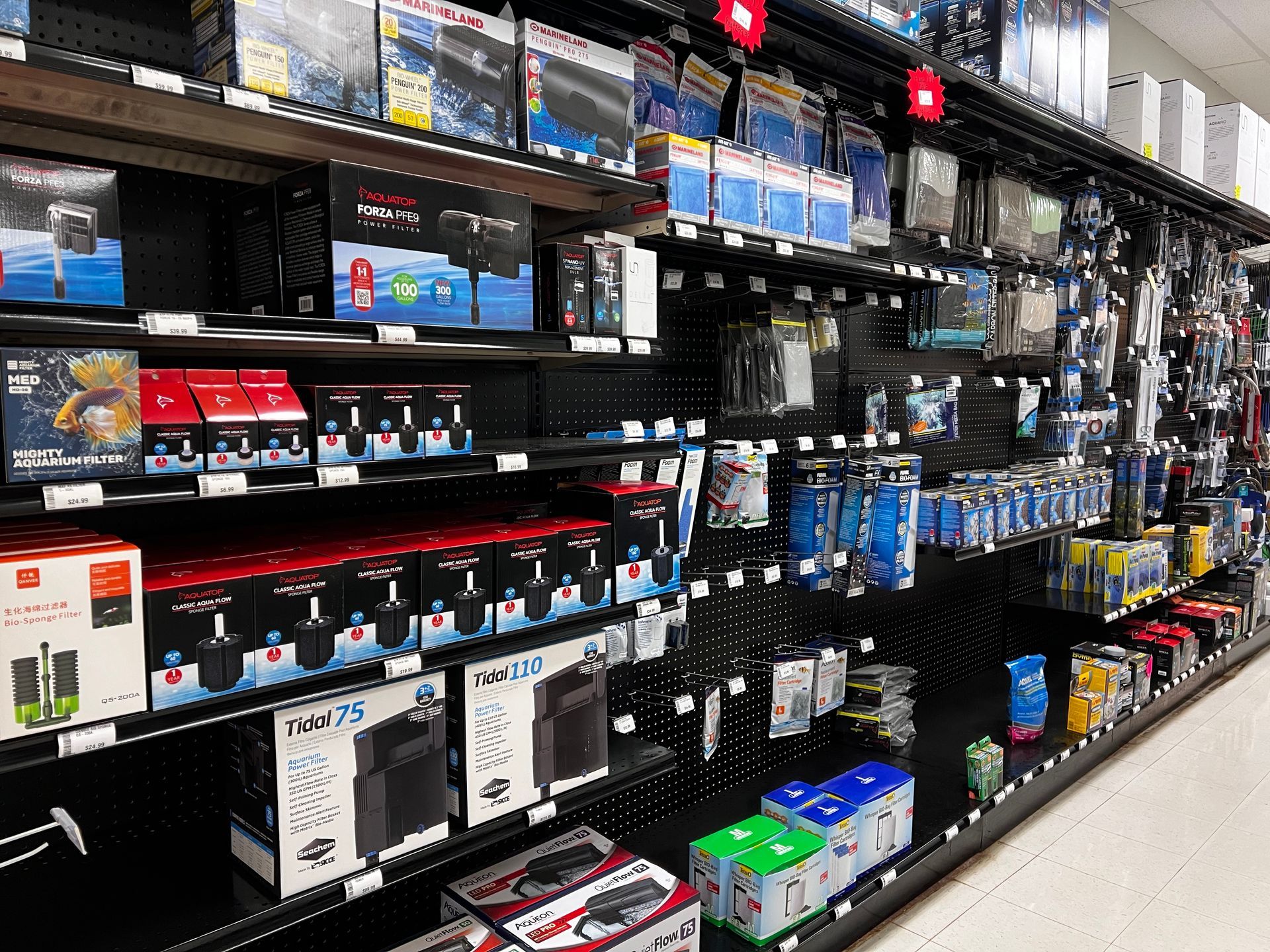 Store aisle with shelves of electronics accessories and boxed products, mostly black and blue packaging.