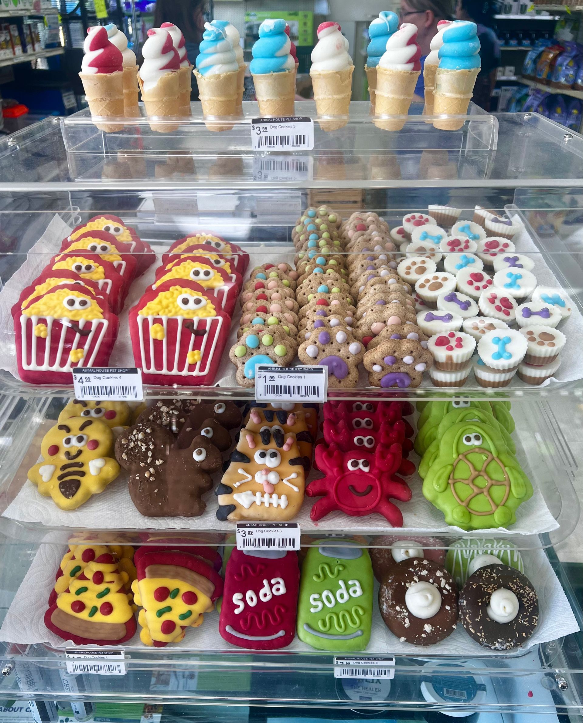 Tray of decorated ice cream cones, cupcakes, and cookies in a dessert display case.