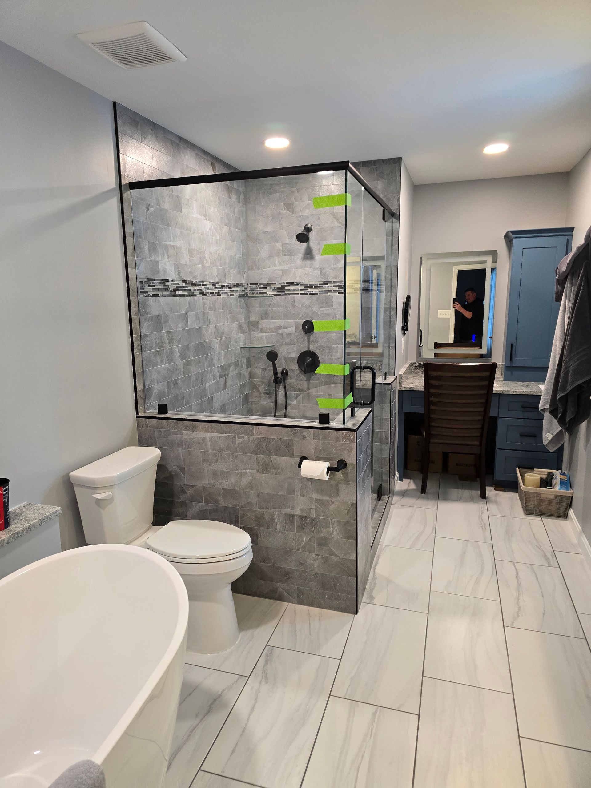 Modern bathroom with a glass shower, toilet, vanity, and a freestanding tub. Gray and white color scheme.