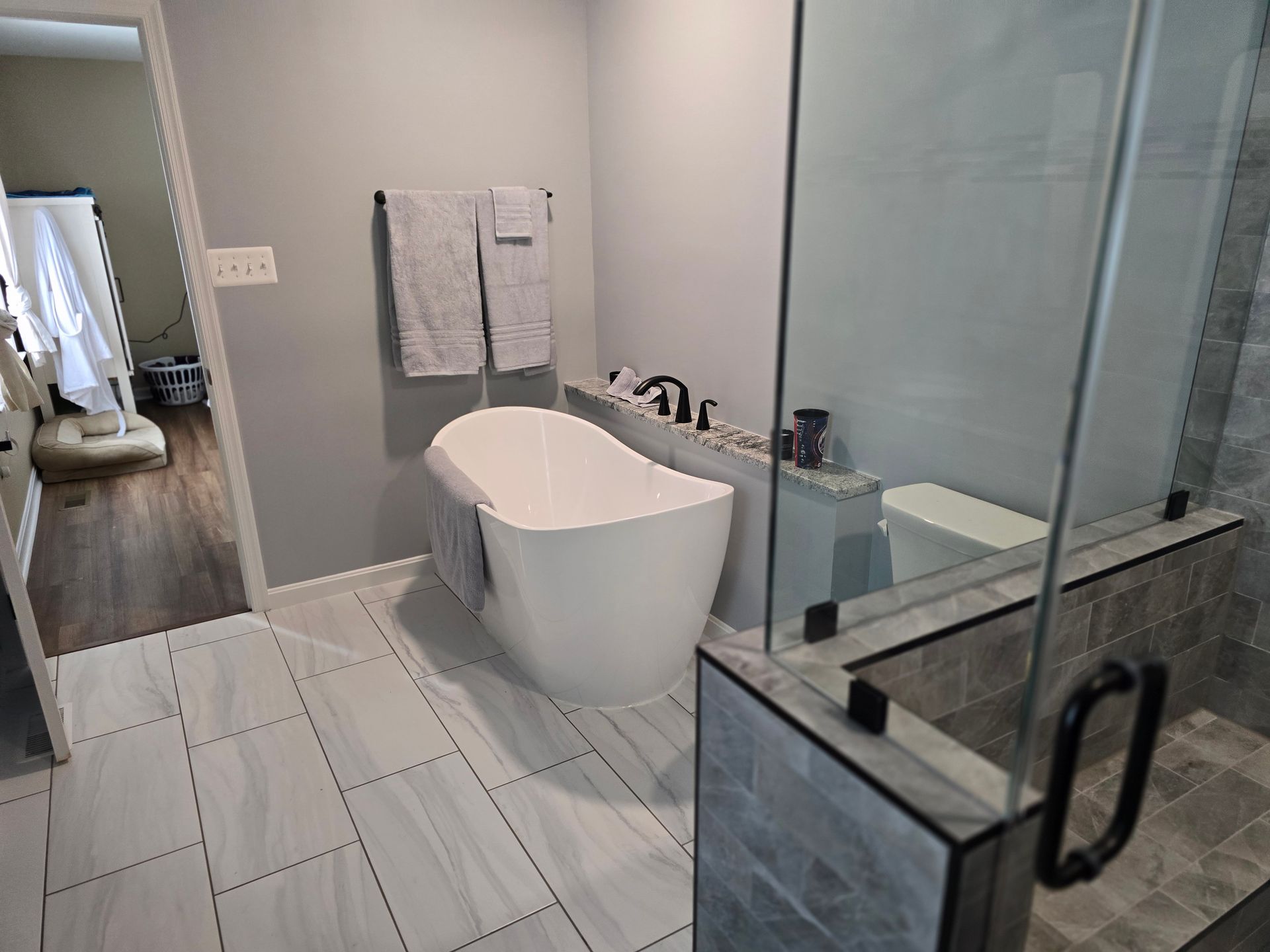 Modern bathroom with a white tub, glass shower, gray walls, and tile floor.