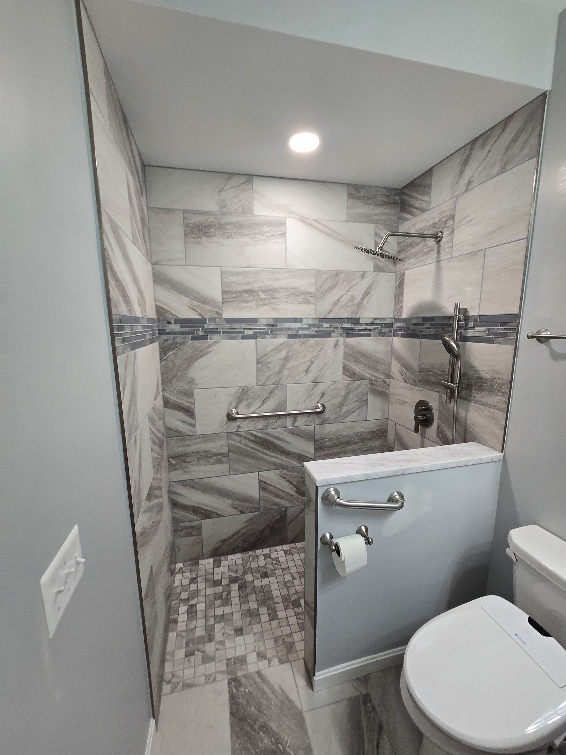 Accessible shower with grab bars, tiled walls, and toilet in a modern bathroom.