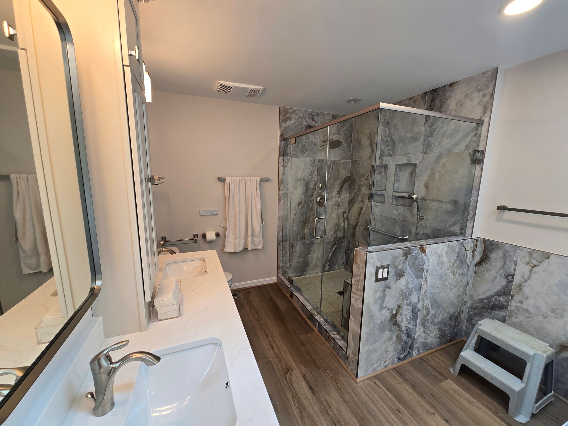 Bathroom with a gray marble shower, double sink, and light wood floors.