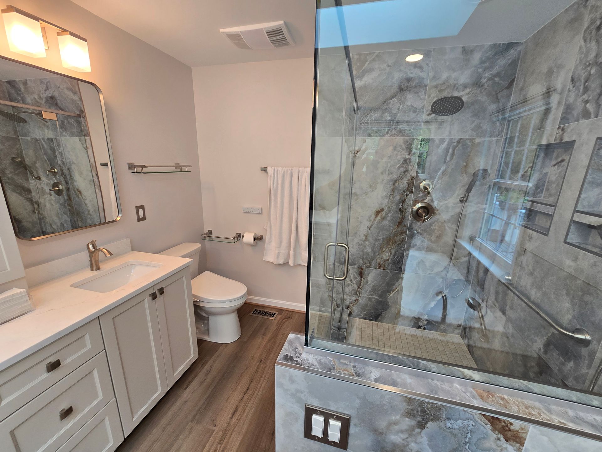 Bathroom with gray tiled shower, white vanity, and wood-look flooring.