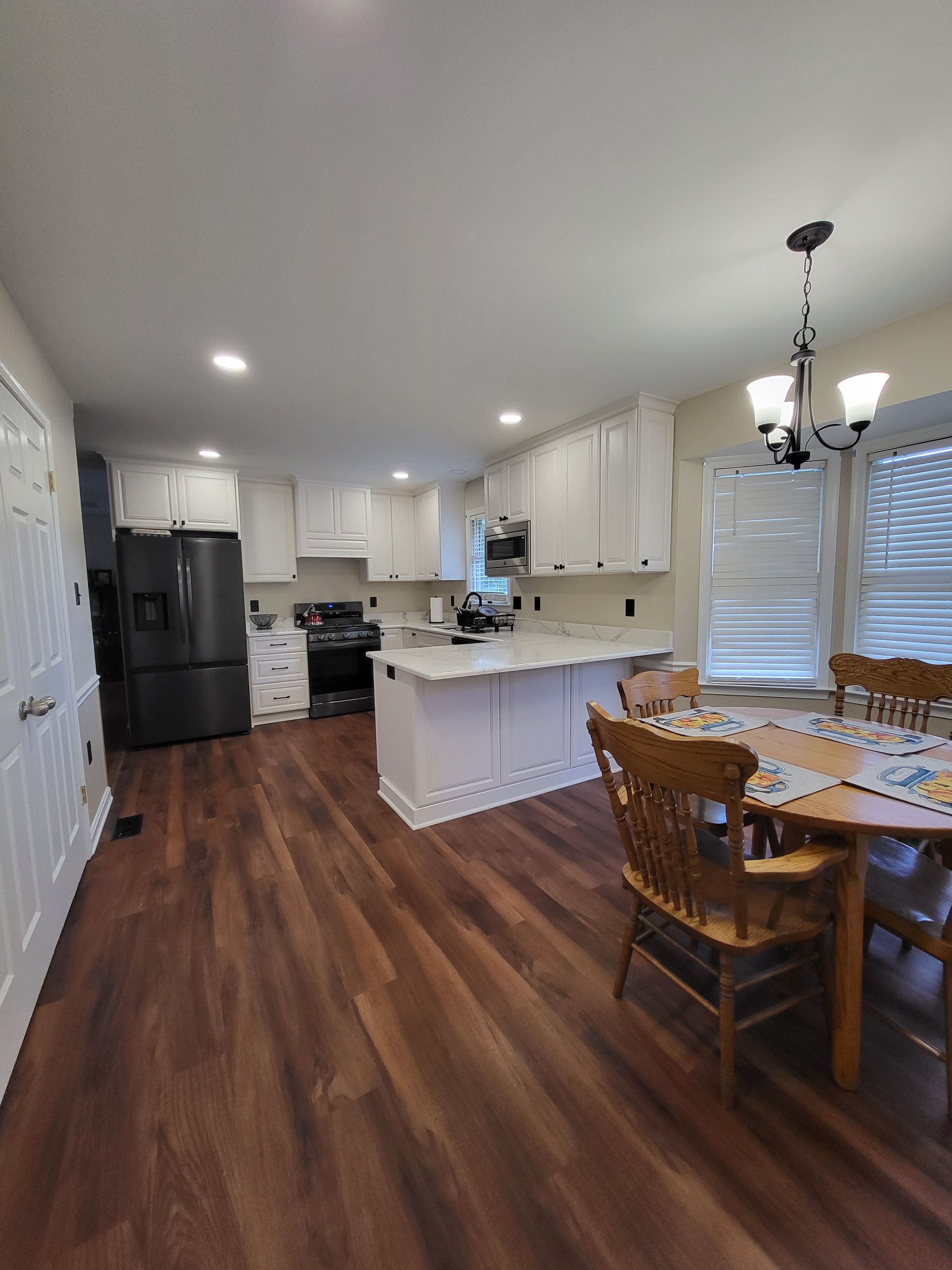 Spacious kitchen with white cabinets, dark refrigerator, and island. Wood flooring. Dining table with chairs.