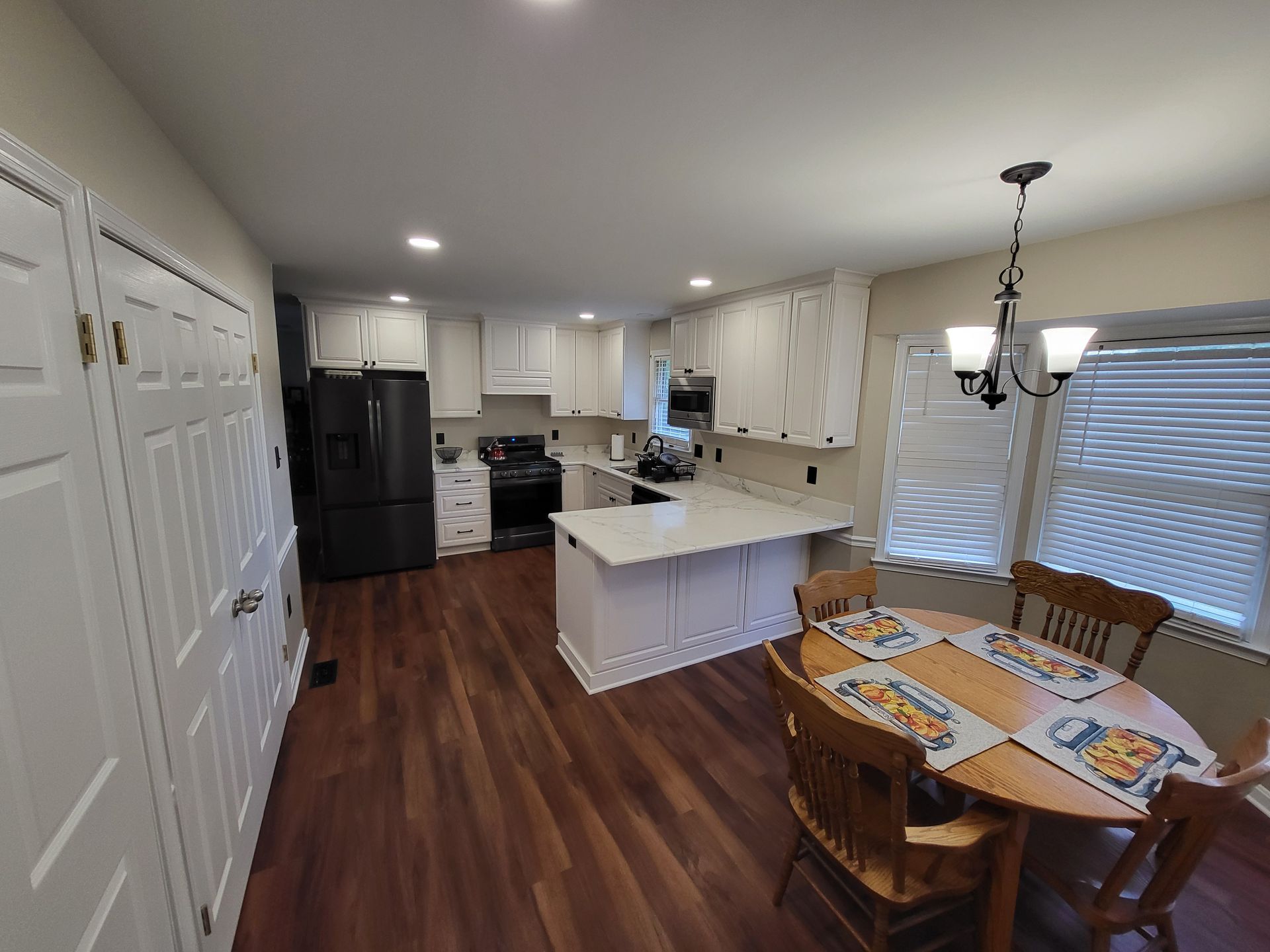 A kitchen with white cabinets, dark refrigerator, and a wooden table. Hardwood floor.