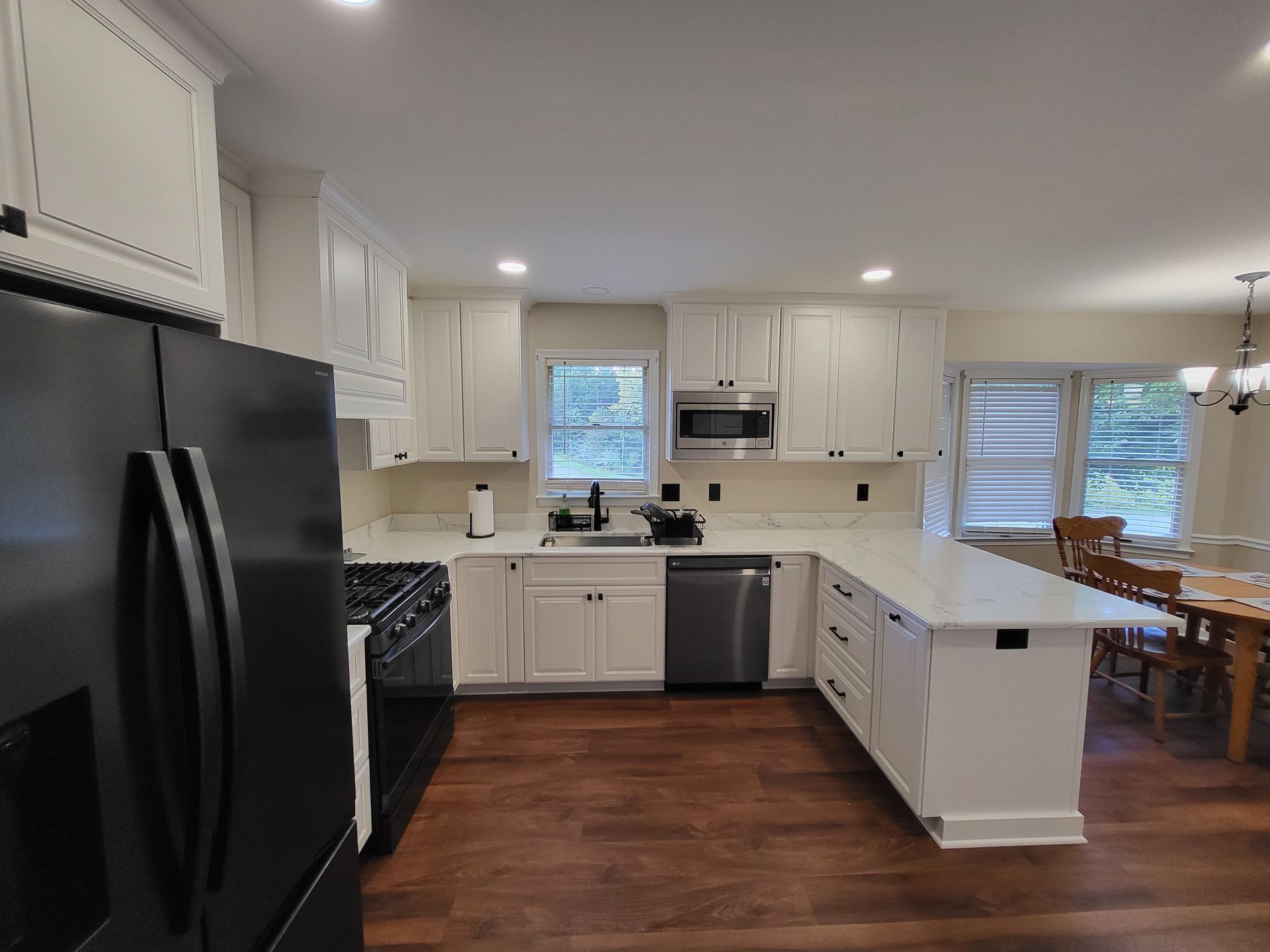 White kitchen with dark appliances, light countertops, and wooden floors.