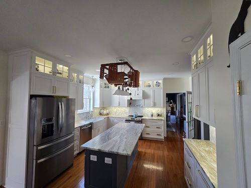 Bright modern kitchen with white cabinets, wood floors, marble island, and stainless steel fridge