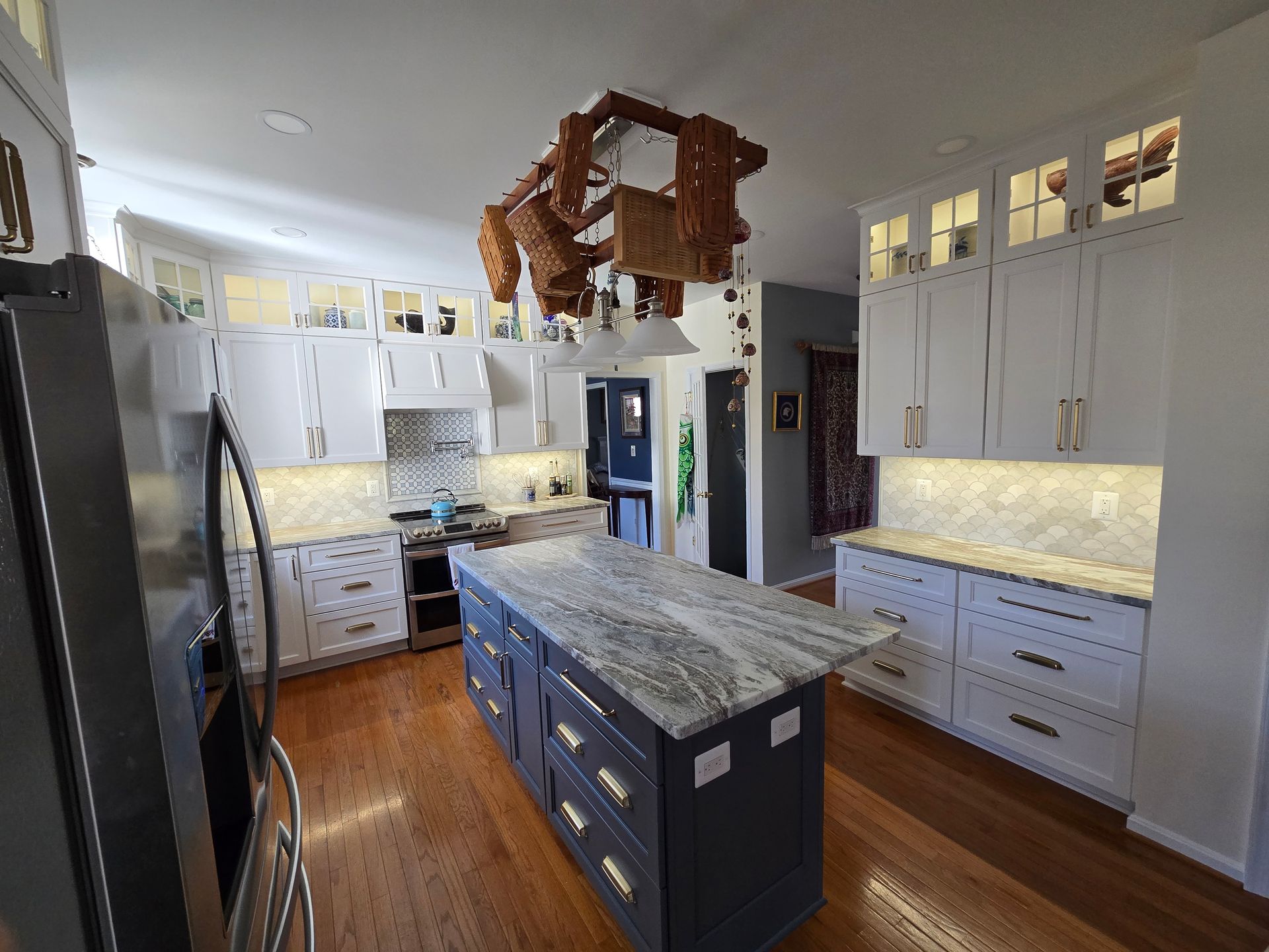 Bright kitchen with white cabinets, blue island, granite counters, and wood floors under a hanging light fixture